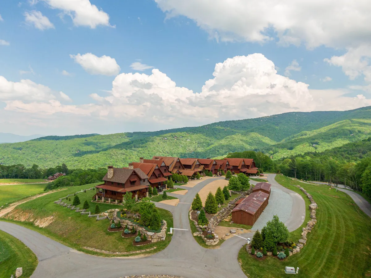 A wide-angle exterior view featuring manicured lawns, large rustic wooden structures, paths for walking, and a breathtaking mountainous landscape in the background. The openness offers a glimpse of the various spaces where families can hike, play, or simply relax outdoors.