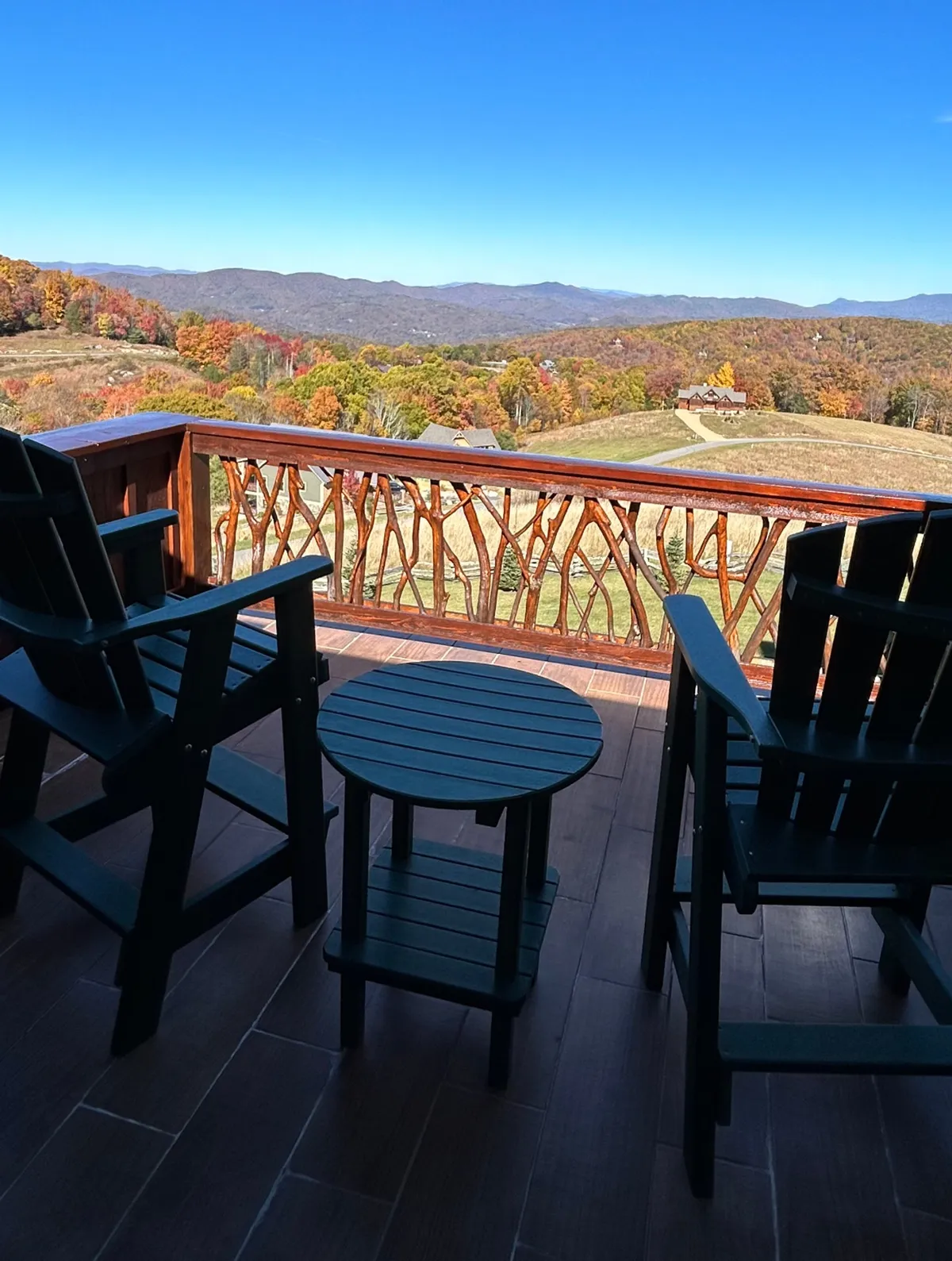Overlooking a mountainous landscape, this image showcases a wooden deck with two Adirondack chairs and a small table. The design highlights opportunities for peaceful moments, such as morning coffee or stargazing, with an unobstructed view of the mountain scenery. The intricate railing adds a touch of rustic charm.