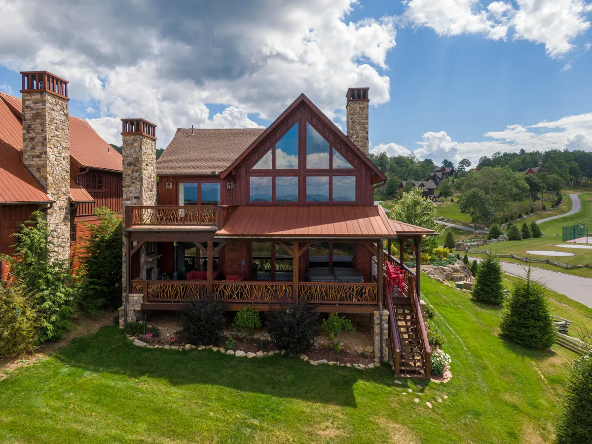 This image features the lodge's exterior with large windows, a prominent stone chimney, and a spacious wooden deck, all set against a scenic natural backdrop. The outdoor deck area is inviting, suggesting ample space for group gatherings and social activities while enjoying the mountain air.