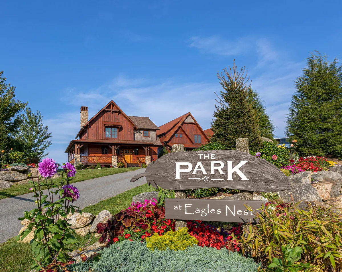 An exterior shot showing the property entrance with a welcoming sign, the house, and vibrant flower beds. The mood is inviting, suggesting community events and a connection to the larger resort environment.